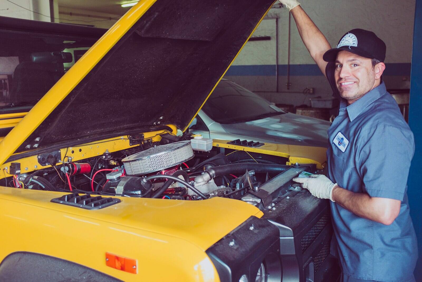Smiling technician working on a vehicle with the hood open