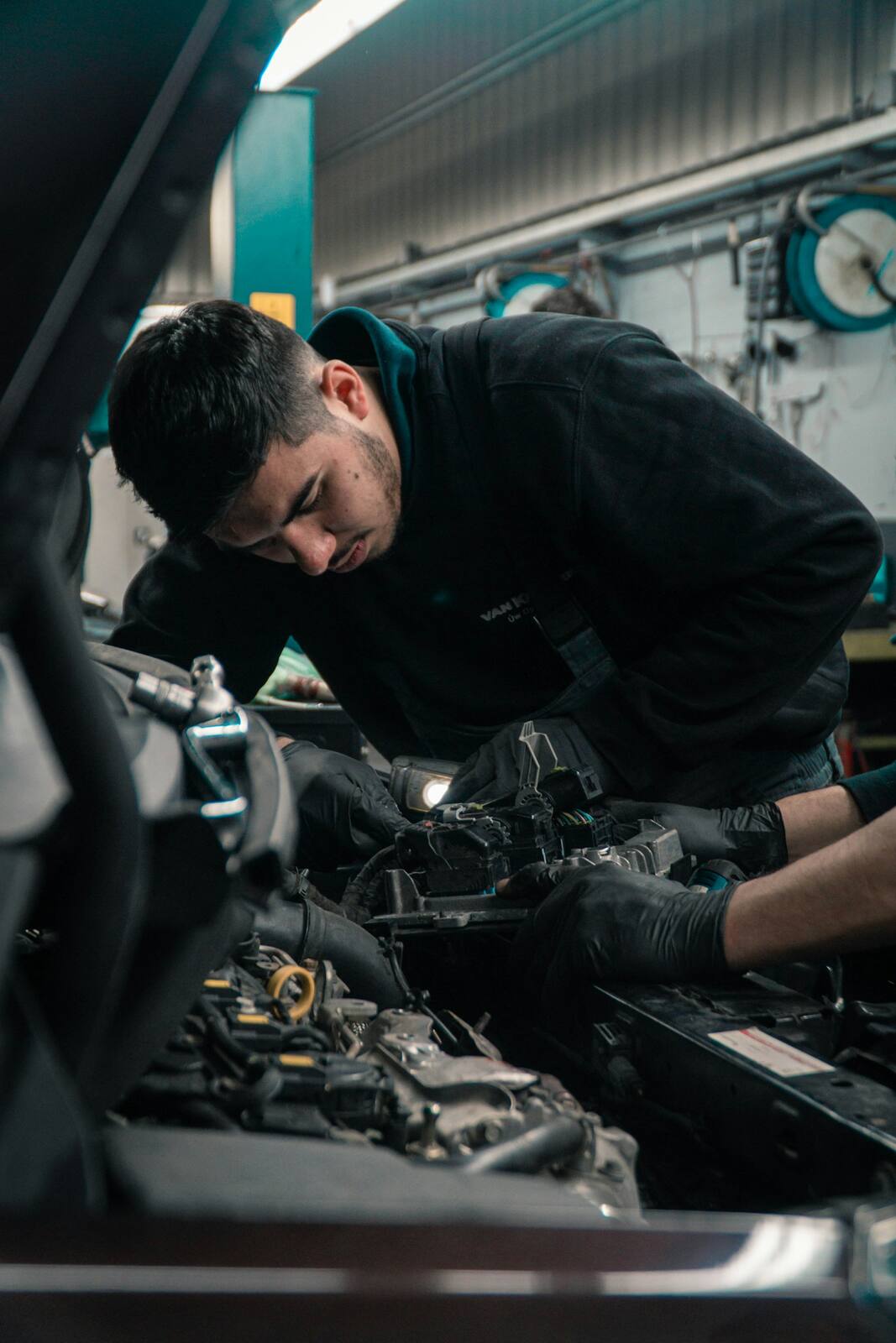 Technician working under the hood of a vehicle in a service bay